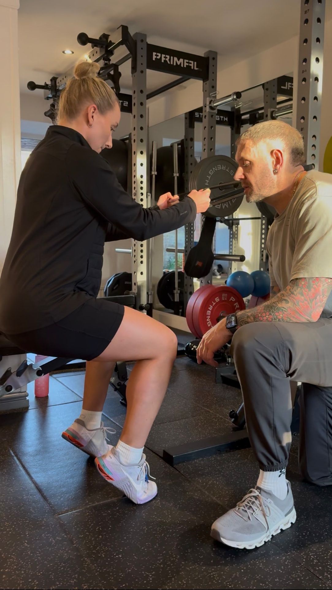 Kate performing a loaded step-up with a barbell while a coach monitors technique