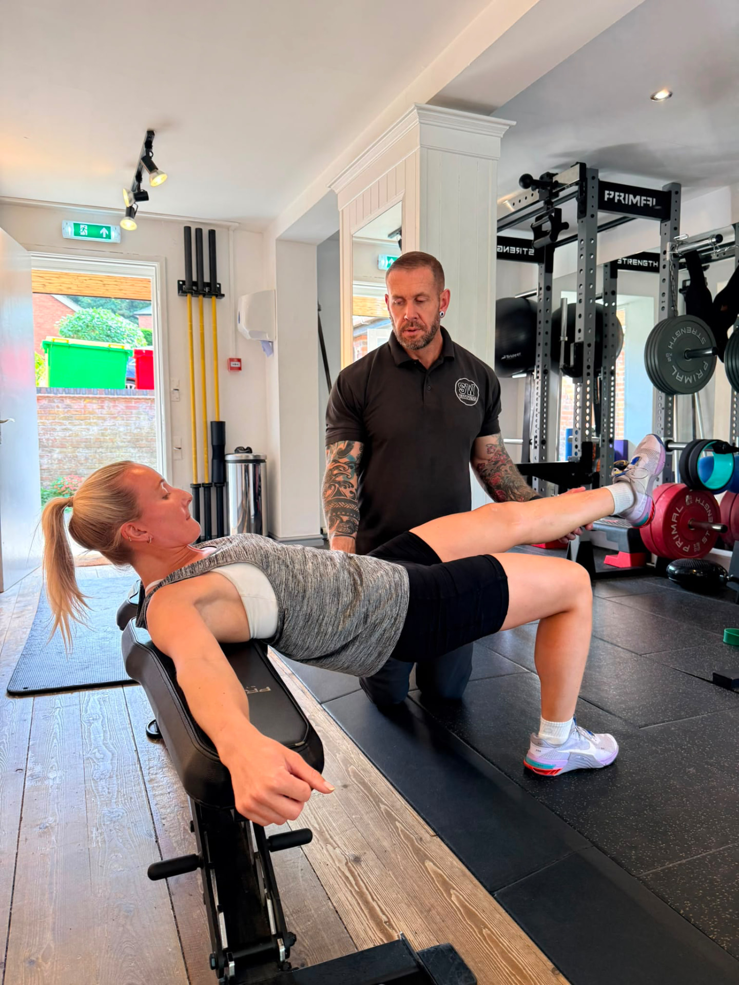 Kate performing a bench-supported single-leg bridge with coaching assistance