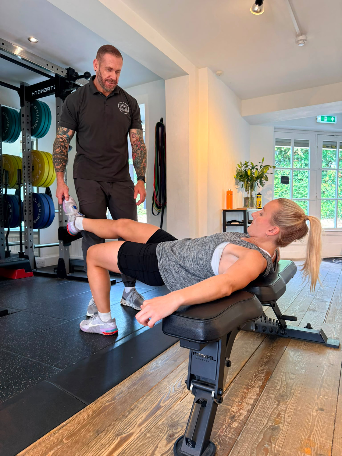 Coach supporting Kate through a single-leg hip bridge on a bench